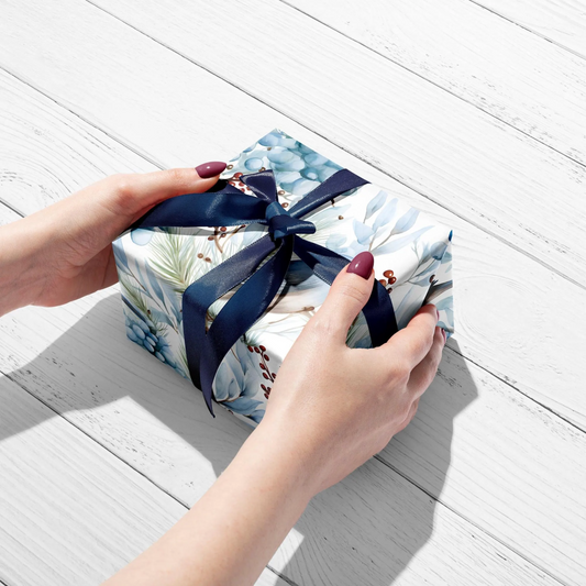 Hand holding a small gift box with floral design and blue ribbon on a light wooden surface