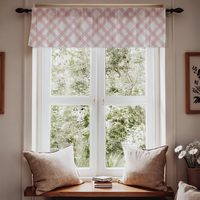 Window with pink checkered valance, white pillows on a wooden bench, and a view of greenery outside.